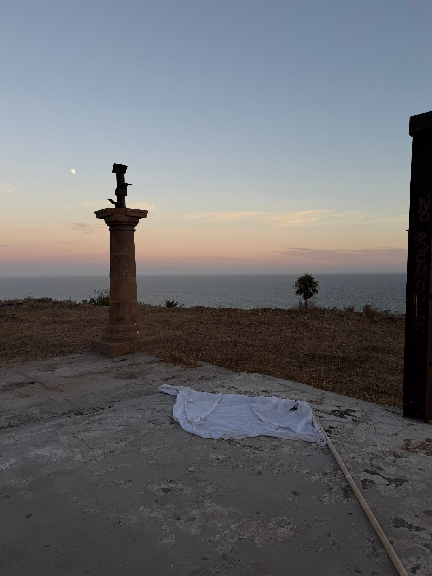 stone column on a cliff at sunset, white flag on the ground